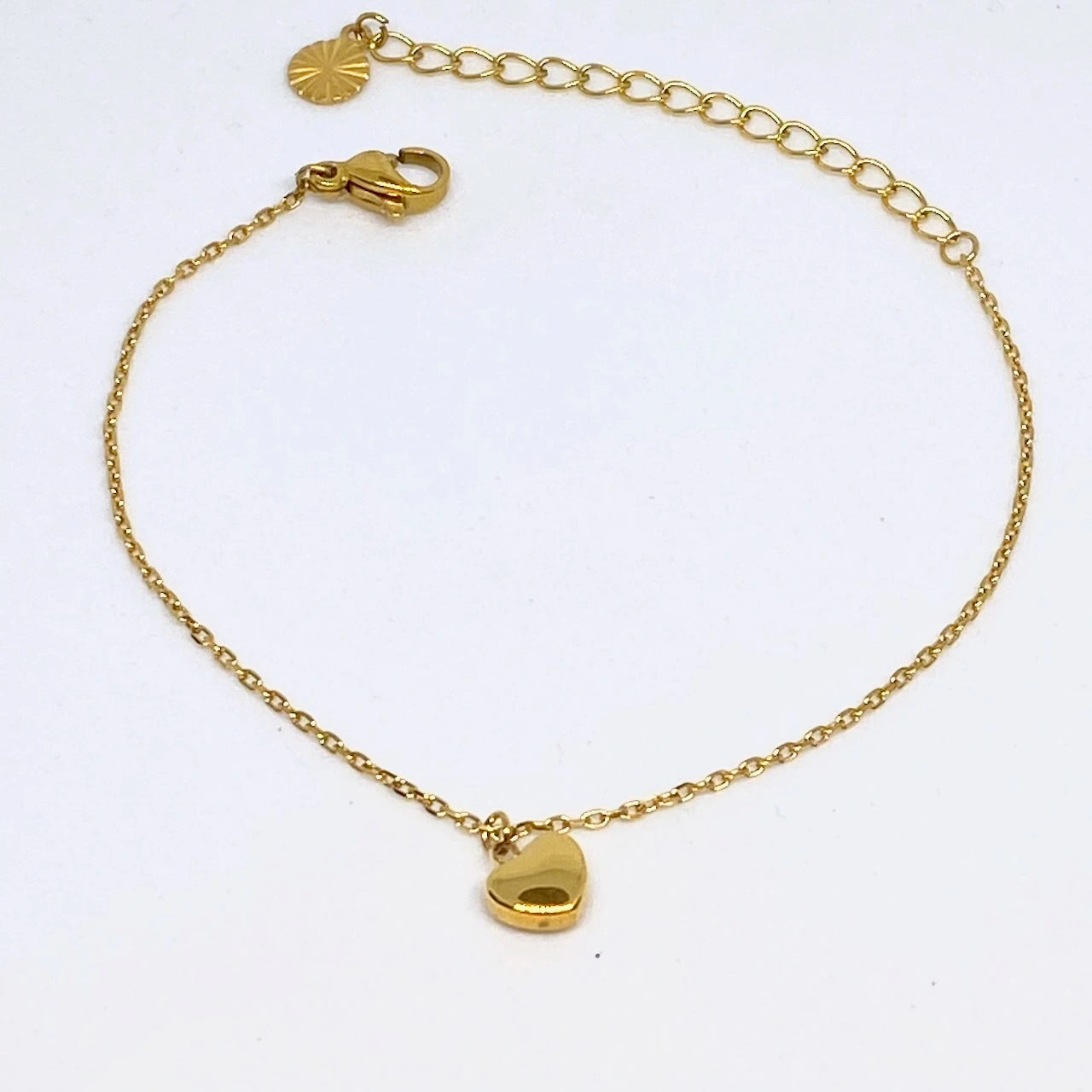 Gold chain bracelet with a heart-shaped charm on a white background